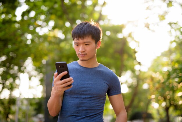 Portrait of young Asian man using phone at the park outdoors