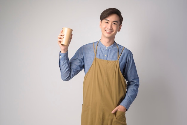 Portrait of young asian man wearing apron holding paper cup over white