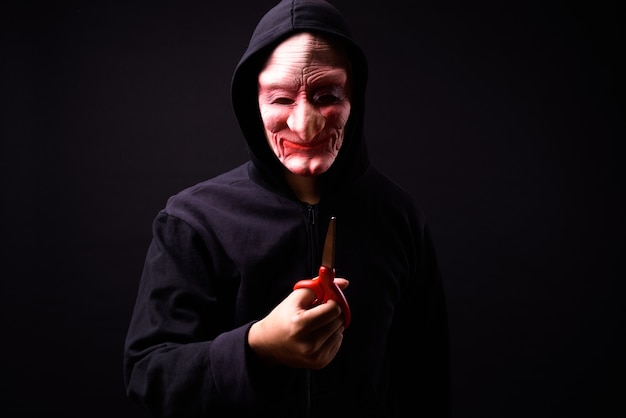 portrait of young Asian man with hoodie and horror mask on black