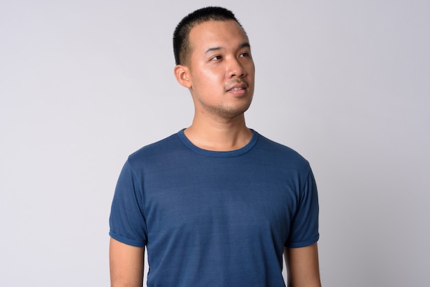 Portrait of young Asian man with short hair against white wall