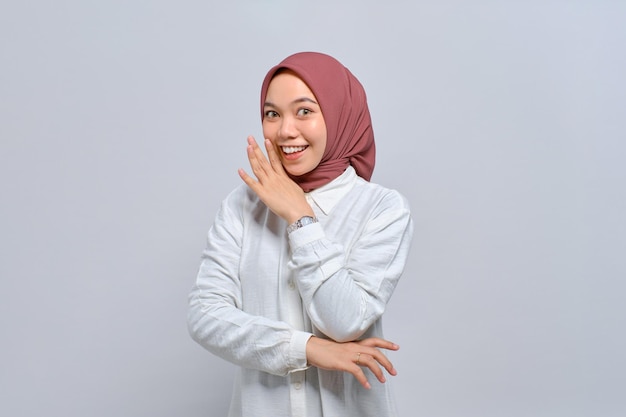 Portrait of young Asian Muslim woman hand near mouth telling secrets and whispering gossip isolated over white background