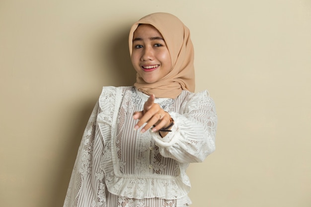 Portrait of young Asian muslim woman wearing hijab smiling while pointing forward