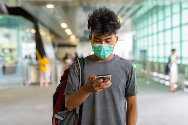 Portrait of young Asian tourist man as backpacker with mask for protection from coronavirus outbreak at the sky train station