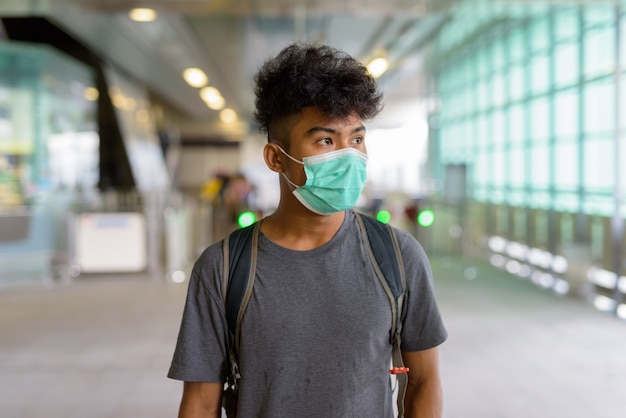 Portrait of young Asian tourist man as backpacker with mask for protection from coronavirus outbreak at the sky train station