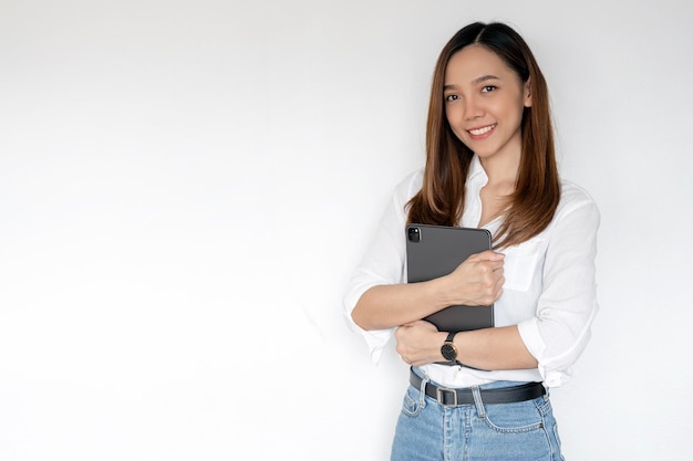 Portrait of young asian woman company worker in casual wear smiling and holding digital tablet standing over white background