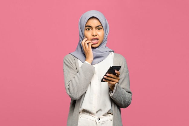 Portrait of young Asian woman looking scared and holding mobile phone