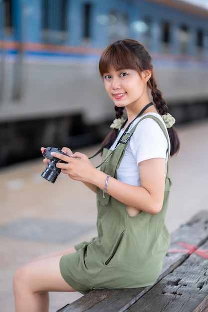 Portrait Young asian woman smiling tourist Traveler girl walking and with a holding the camera waits train travel journey is taken in railway platform Thailand summer relax vacation Concept