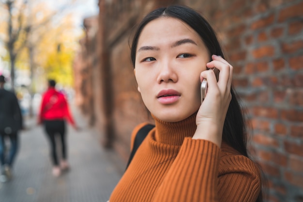 Portrait of young Asian woman talking on the phone outdoors in the street. Urban and communication concept.