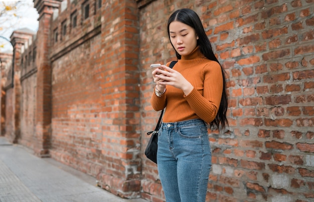 Portrait of young Asian woman using her mobile phone outdoors in the street. Urban and communication concept.