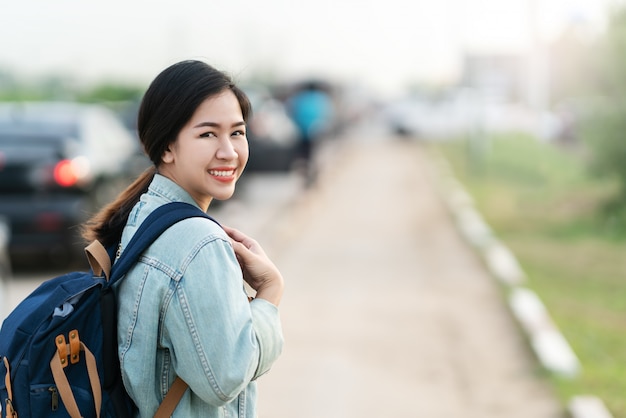 Portrait of young asian woman wearing blue denim jacket and backpack smiling looking back 