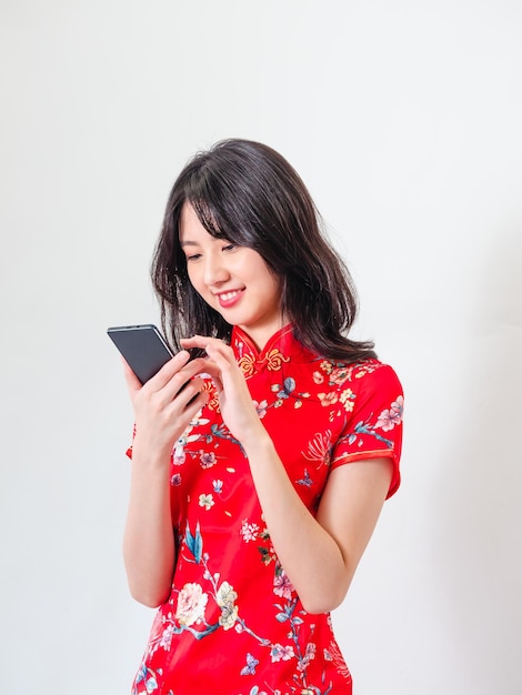 Portrait of a young asian woman wearing traditional cheongsam qipao dress using smartphone on white background