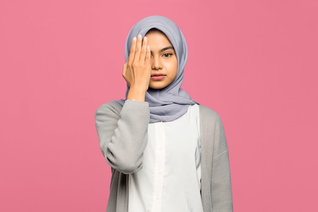 Portrait of young Asian woman with her closed hides half of her face with her palm