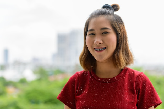 Portrait of young Asian woman with short hair against view of the city outdoors