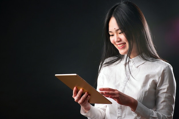 Portrait of a young Asian woman with a tablet on a black background