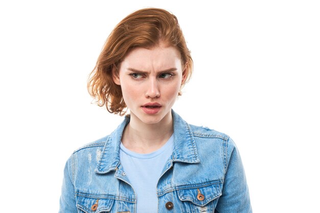 Portrait of young attractive beautiful thoughtful redhead female student thinking looking at copyspace, isolated on white background. Woman in blue jeans