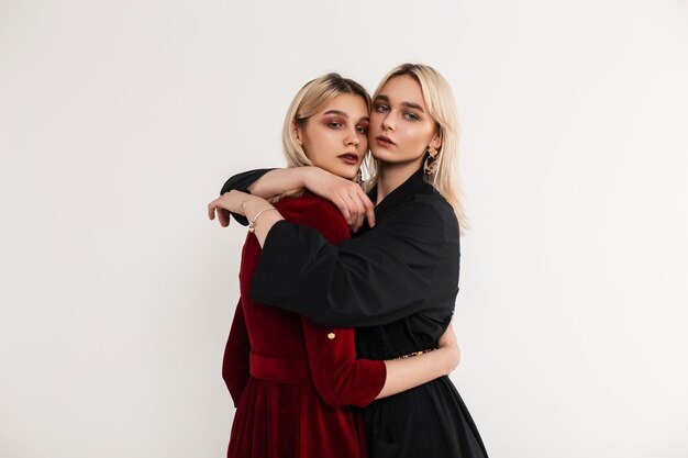 portrait young attractive blondes sisters women in stylish red-black fashionable dresses near gray vintage wall in room