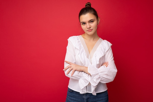 Portrait of young attractive caucasian hipster woman in trendy casual clothes. Sexy carefree female person posing isolated near red wall in studio. Positive model with natural makeup. Empty space.