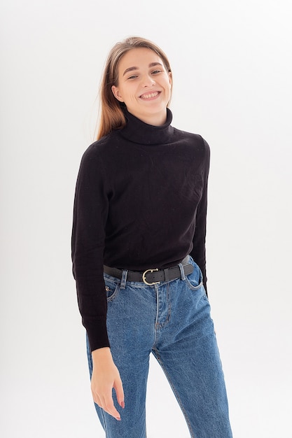 Portrait of young attractive caucasian woman with long hair in black turtleneck, blue jeans isolated on white studio background. skinny pretty female posing on cyclorama. model tests of beautiful lady