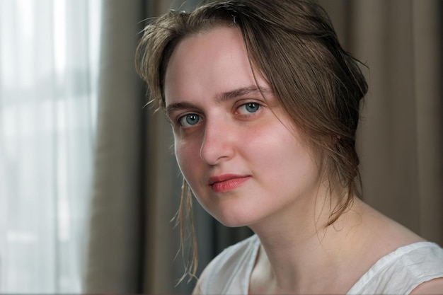 Portrait of a young attractive girl in a white shirt on a light background closeup