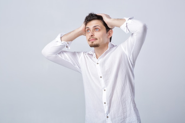 Portrait of young attractive surprised brunette male in white shirt on gray background.