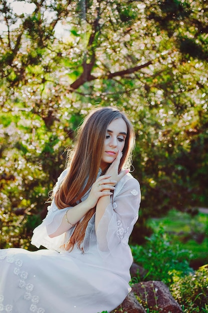 Portrait of young attractive woman in long white wedding dress in spring garden with blooming trees.