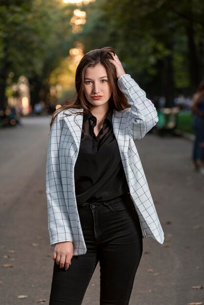 Portrait of young attractive woman in park Beautiful girl in plaid jacket Spring warm day Stylish brunette girl