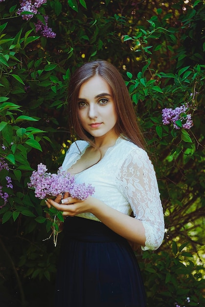 Portrait of young attractive woman in spring garden with a bouquet of lilacs. Spring background.