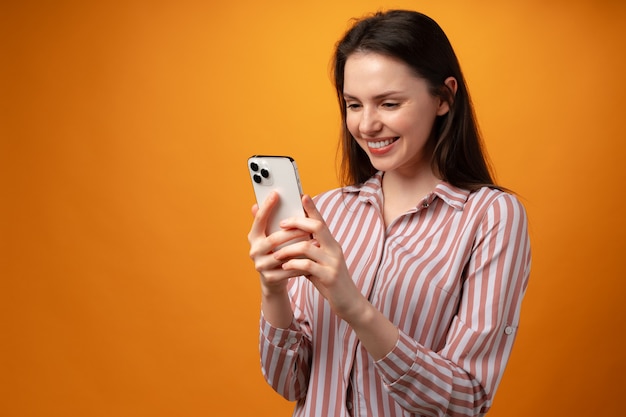 Portrait of young attractive woman using her smartphone against yellow surface