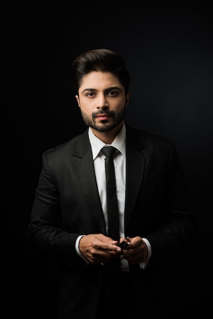 Portrait of young bearded Indian businessman against black background, moody lighting