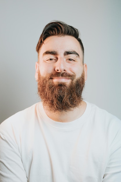 Portrait of a young bearded man smiling to camera with a white background. Cinematic tones and lightning. Happy day, mental health concept, depression and anxiety