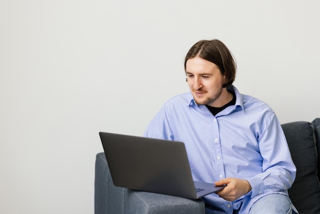 Portrait of young bearded man smiling and using laptop while sitting on sofa at home