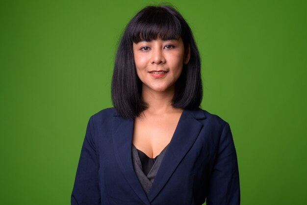 Portrait of young beautiful Asian businesswoman against green wall