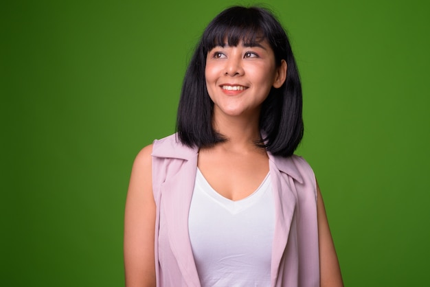 Portrait of young beautiful Asian businesswoman against green wall