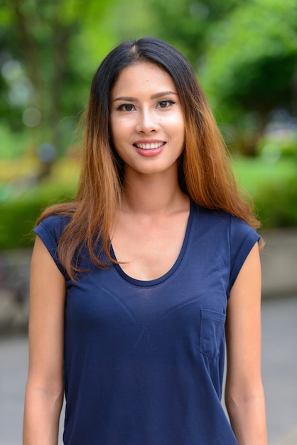 Portrait of young beautiful Asian businesswoman relaxing at the park outdoors