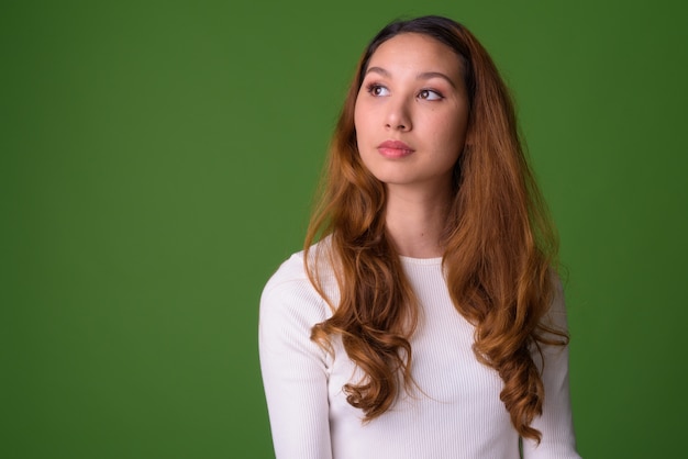 Portrait of young beautiful Asian woman against green wall