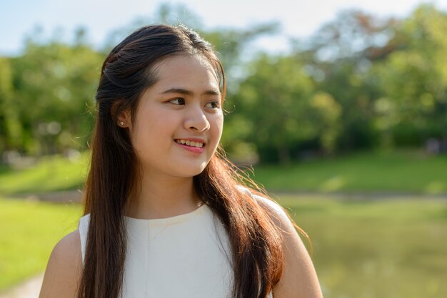 Portrait of young beautiful Asian woman relaxing at the park outdoors