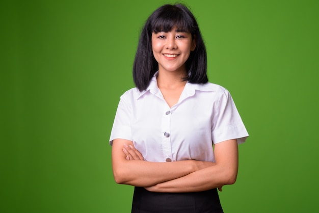 Portrait of young beautiful Asian woman student against green wall