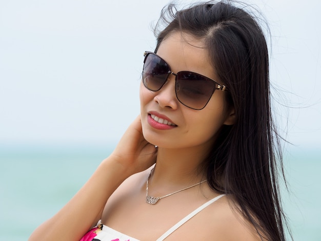 Portrait of young beautiful asian woman wearing sunglasses and standing on the beach. Summer time, relaxation or vacations concept