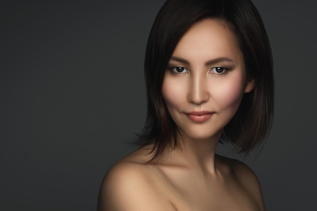 Portrait of young and beautiful asian woman with a short dark hair on gray background