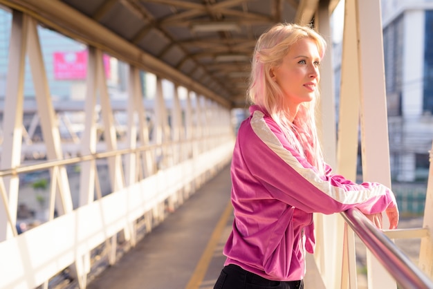 Portrait of young beautiful blonde woman at footbridge in the city outdoors