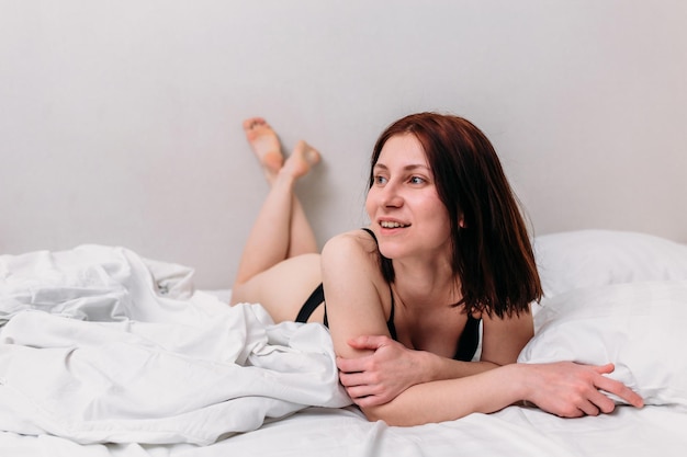 Portrait of a young beautiful brunette lying in bed wearing underwear