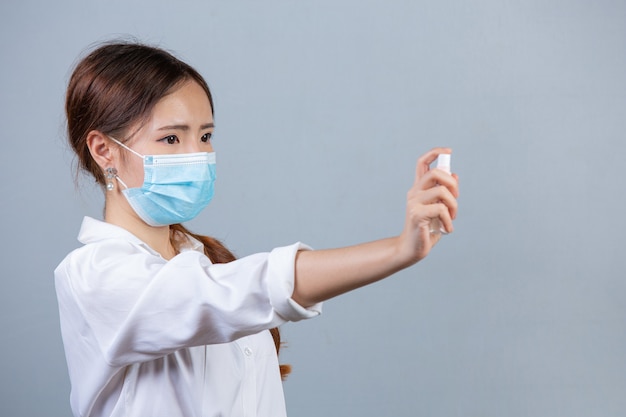 Portrait of young beautiful business woman wearing face mask hands applying alcohol spray  on gray surface