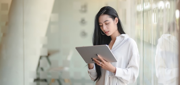 Portrait of young beautiful businesswoman working on her project while using digital tablet in modern office