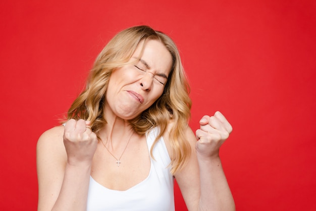 Portrait of young beautiful caucasian woman with medium blonde wavy hair and nude makeup in white t-shirt looks in disgust