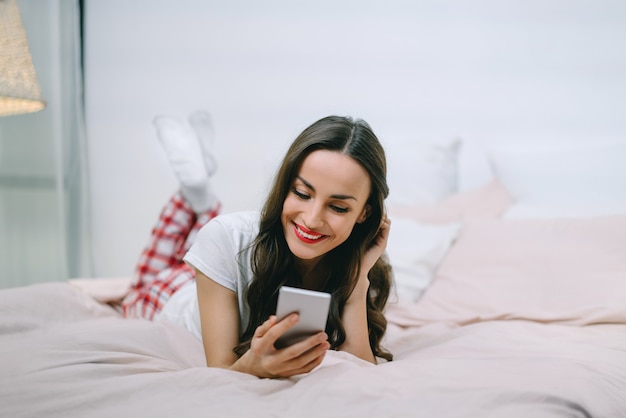 Portrait of a young beautiful dark-haired woman lying in bed browsing her mobile phone