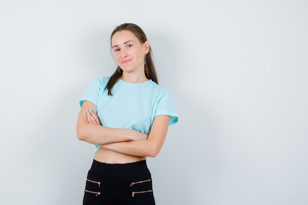 Portrait of young beautiful female with arms folded in t-shirt, pants and looking glad front view