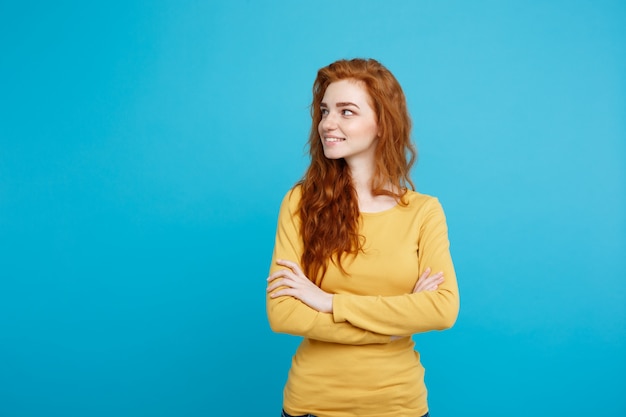 Portrait of young beautiful ginger woman with freckles cheerfuly smiling looking at camera. Isolated on pastel blue background. Copy space.