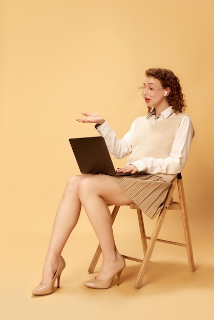 Portrait of young beautiful girl in formal clothes sitting on chair and having online video call on