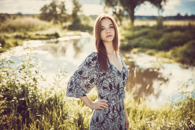 Portrait of a young beautiful girl in a long dress standing on the background of the sky and nature during the sunset