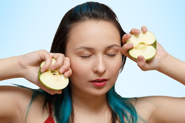 Portrait of a young beautiful girl with two halves of apples in her hands on a blue background